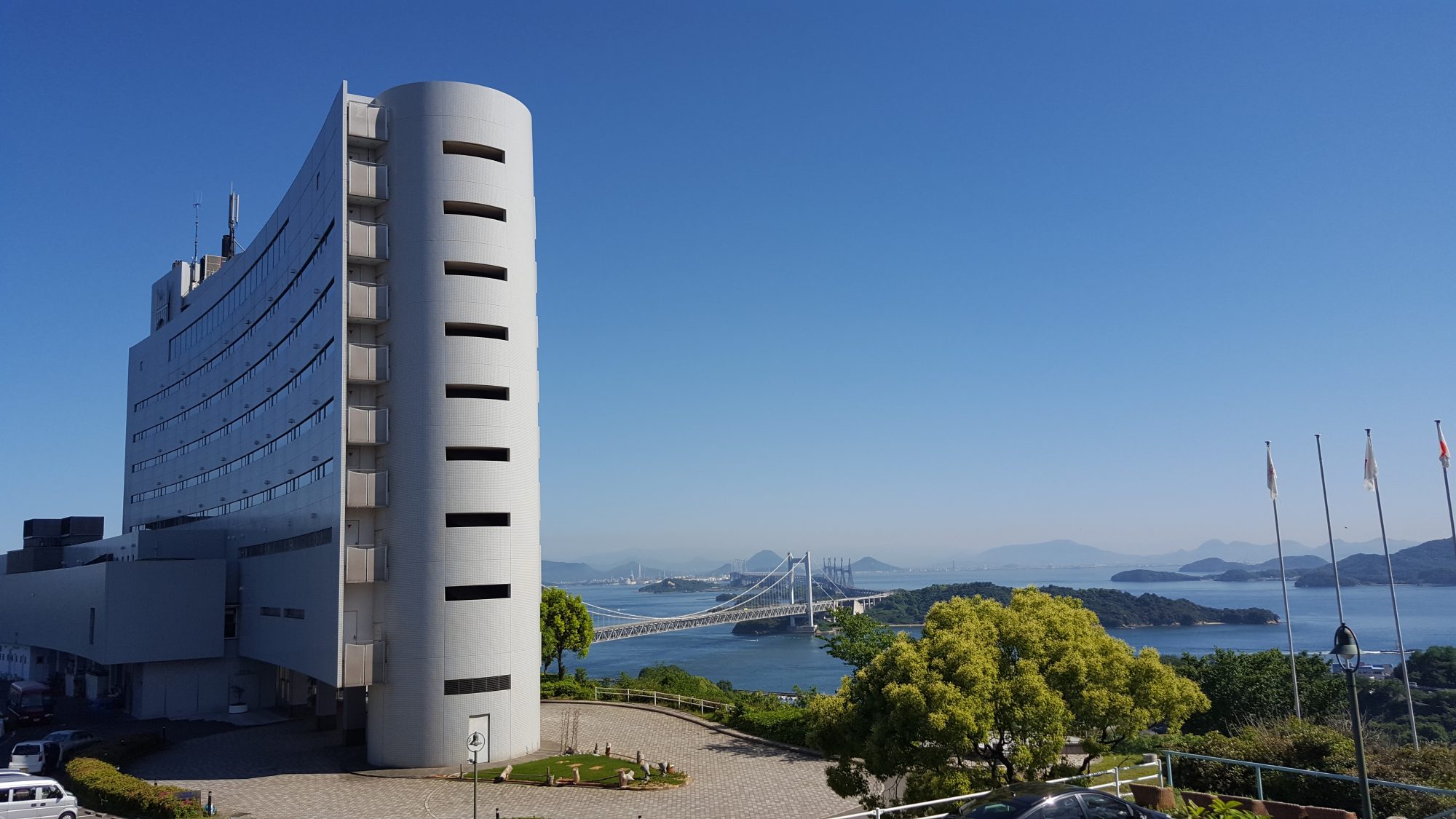 空の青、海の碧、瀬戸大橋と瀬戸内海国立公園の多島美を背景に建つ白亜のリゾートホテル全景。